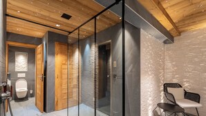 A modern bathroom with a wooden ceiling, glass shower enclosure, and a seating area with a chair and table. - Hameau des clos Téléporté (Les Gets)