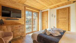A wooden-paneled room with a bed, a TV, a desk, and a chair. - Hameau des clos Téléporté (Les Gets)