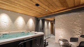 A modern spa area with a hot tub, seating, and a wooden ceiling. - Hameau des clos Téléporté (Les Gets)