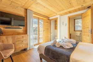 A wooden-paneled bedroom with a bed, a TV, a chair, and a sliding glass door to a balcony. - Hameau des clos Téléporté (Les Gets)