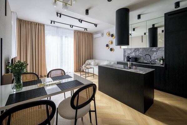 Une cuisine moderne dotée d’un îlot central, un coin repas avec une table et des chaises, et un espace de vie avec un canapé et des rideaux.