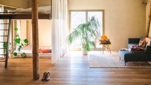 Un salon chaleureux avec un lit superposé, un plancher en bois, une grande plante en pot, un fauteuil jaune et un canapé vert.