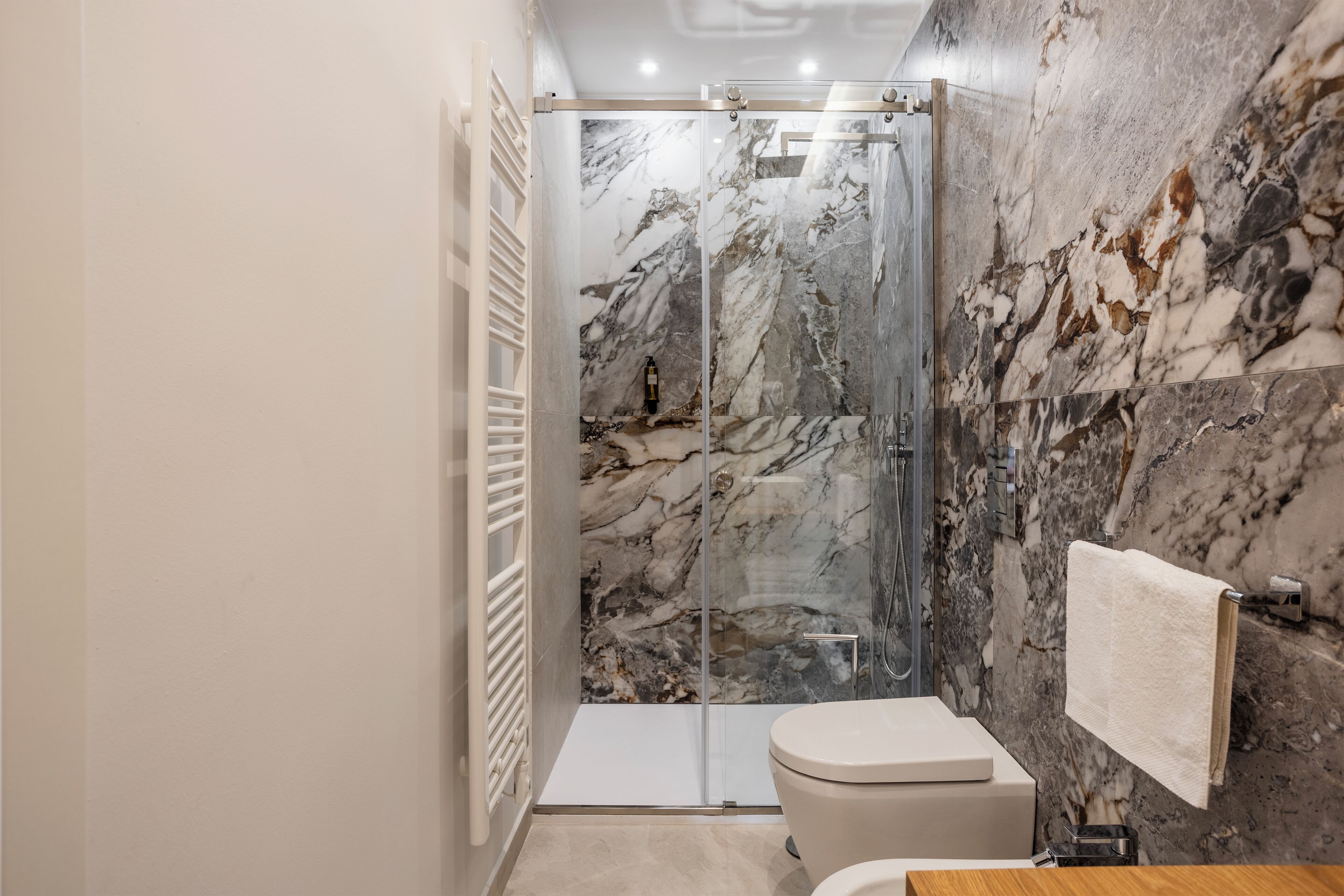 Une salle de bain moderne avec une douche à parois de verre, des murs en marbre, des toilettes et un porte-serviettes.