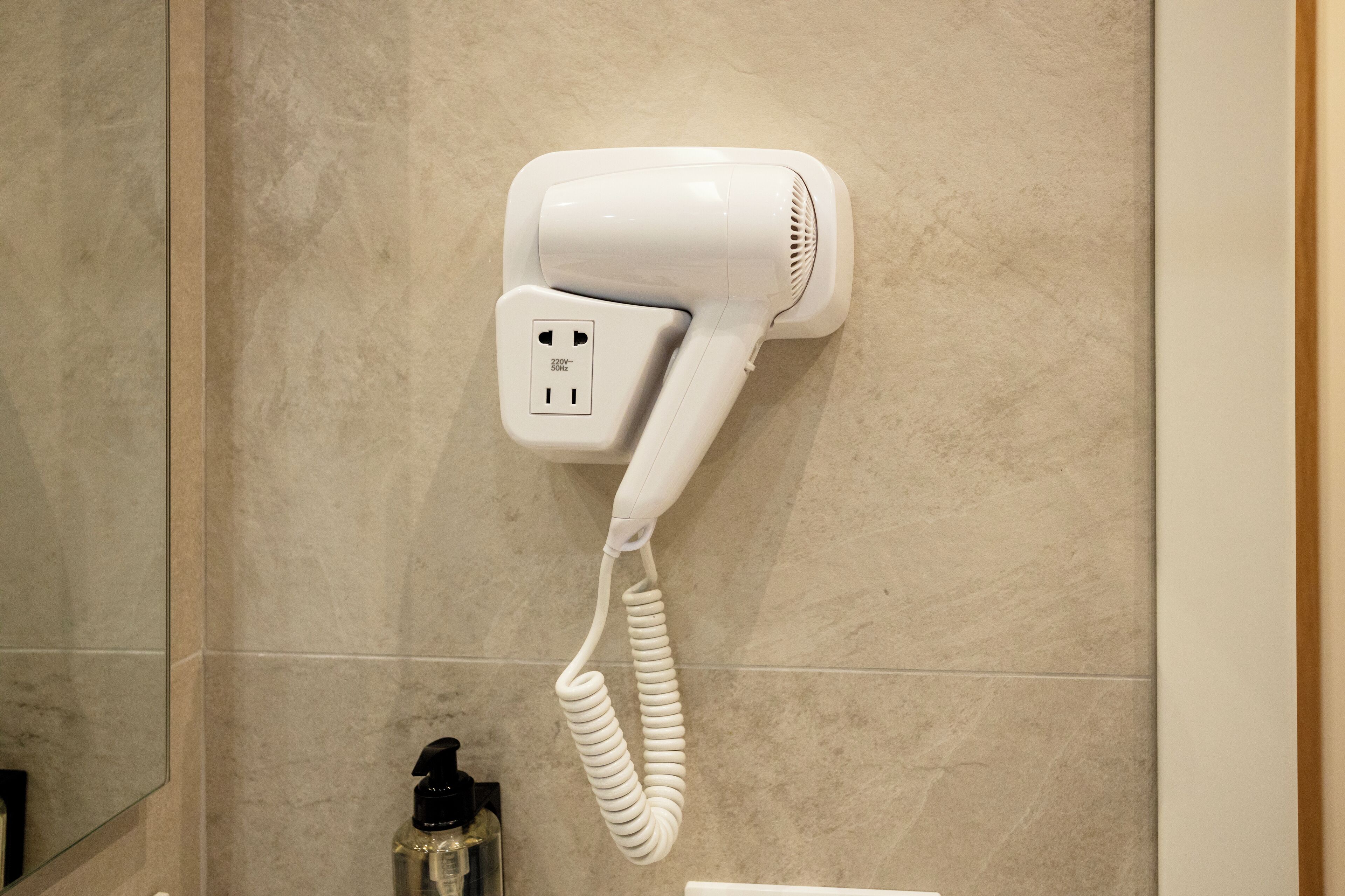 A hair dryer mounted on a wall in a bathroom with tiled flooring.