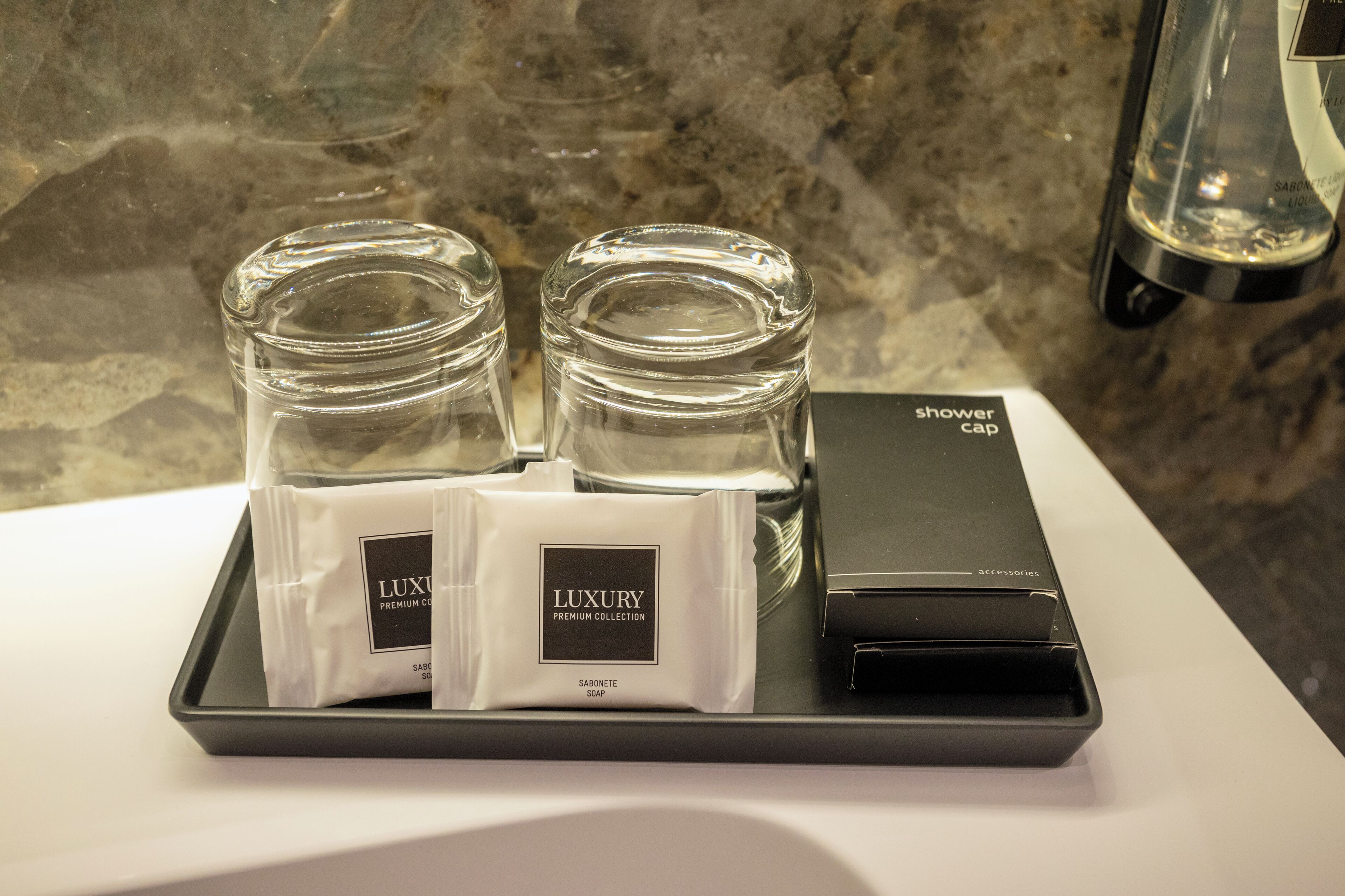 A tray with two glass bottles and two white bags labeled "LUXURY PREMIUM COLLECTION" on a bathroom counter.