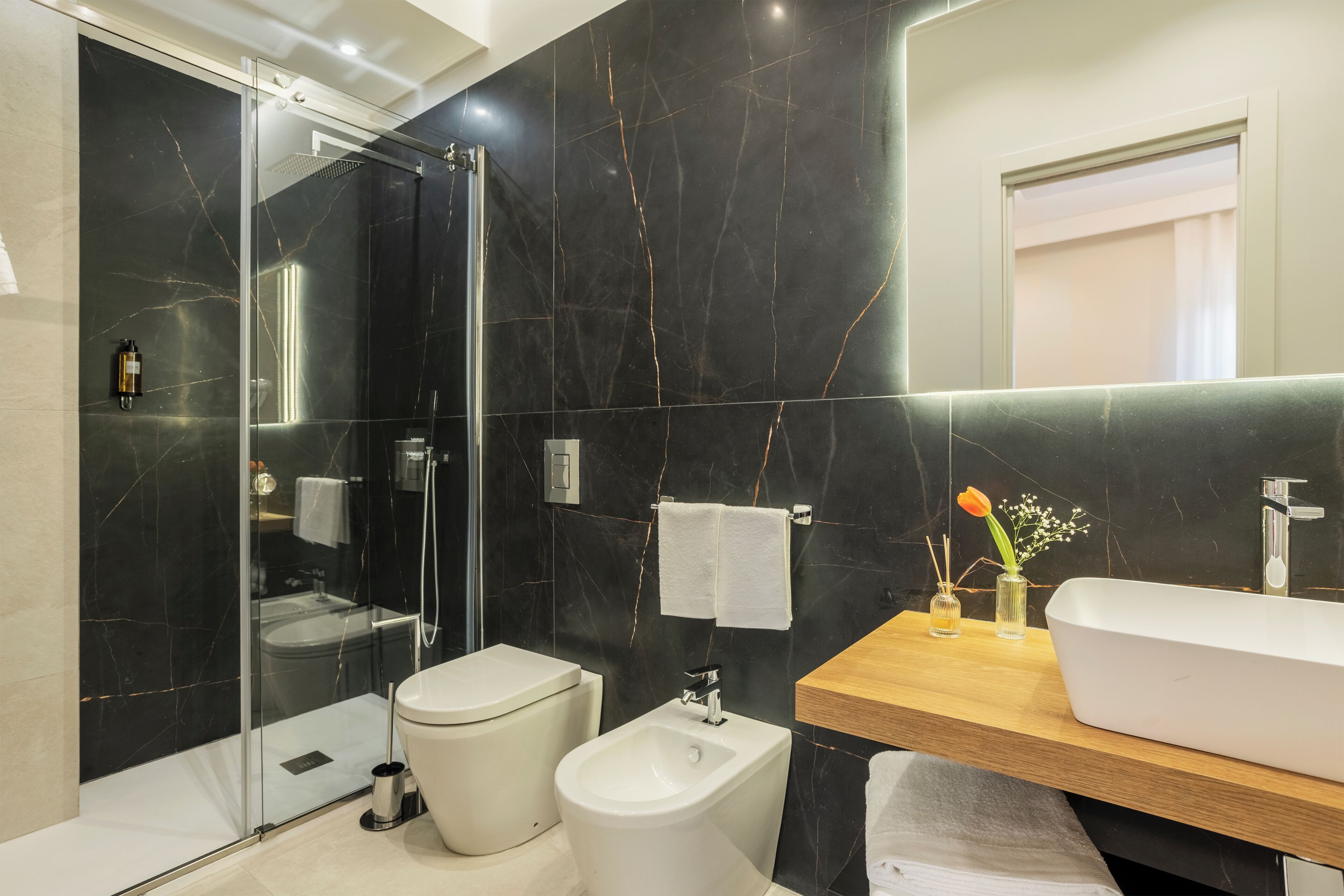 Un baño moderno con ducha de vidrio, un bidé, un tocador de madera con lavamanos y un espejo.