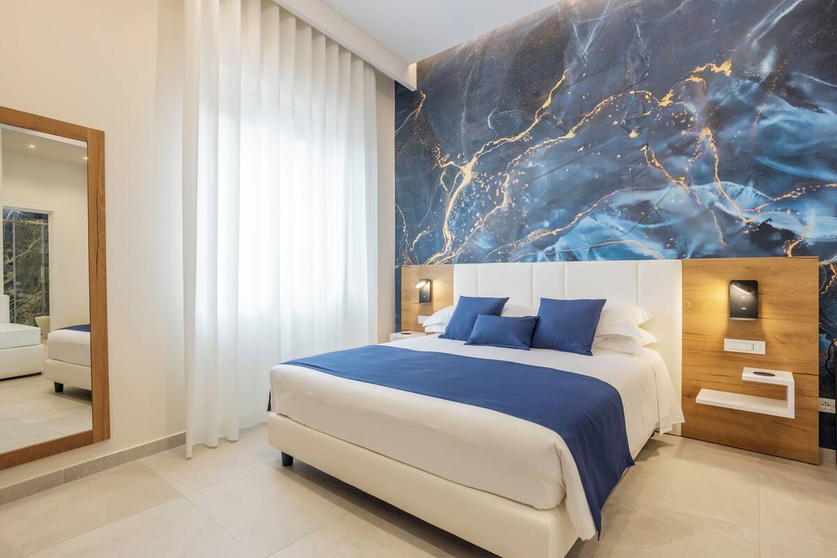 Ein modernes Schlafzimmer mit einem großen Bett, einem Wand-Fernseher und einem Wandbild im Marmor-Stil.