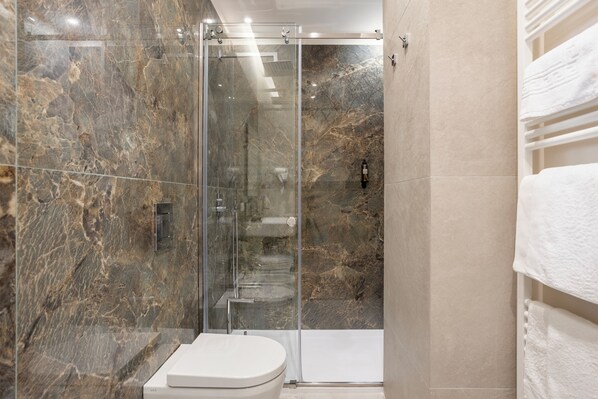A modern bathroom with a glass-enclosed shower, marble walls, and a white toilet. - Julia's Boutique Rooms (Palermo)