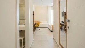 Une chambre d’hôtel moderne, équipée d’un lit, d’un bureau, d’une chaise et d’une salle de bain visible à travers une porte ouverte.