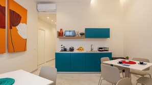 Une cuisine moderne avec des meubles de couleur turquoise, un plan de travail blanc et un coin repas comprenant une table et des chaises blanches.