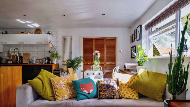 Una sala de estar con sofá, una mesa de comedor y una cocina con ventana.