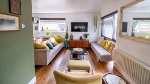 Una sala de estar con un sofá, un reposapiés, una mesa de centro y un televisor montado en la pared.