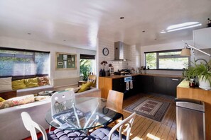 A modern kitchen with a dining area, wooden flooring, and a view of the outdoors.