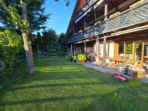Ein zweistöckiges Gebäude mit überdachter Terrasse, Sitzgelegenheiten im Freien und einem Rasen.