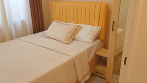 Una cama con cabecera amarilla, cubrecama blanco y dos almohadas.