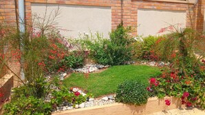 Un jardín bien cuidado con una variedad de plantas y flores, un pequeño césped y un muro de ladrillo al fondo.