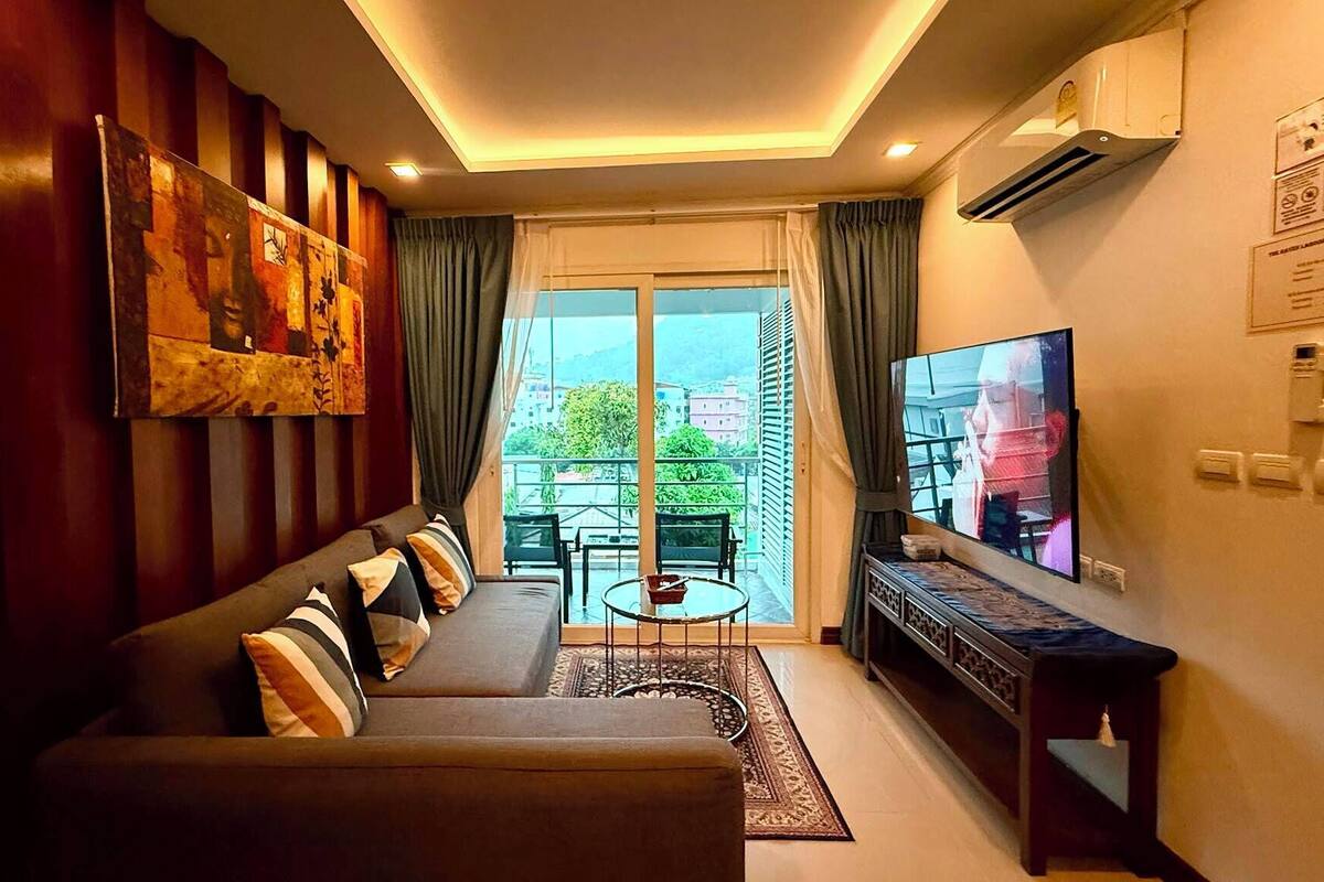 A living room with a sofa, TV, and a balcony with a view.