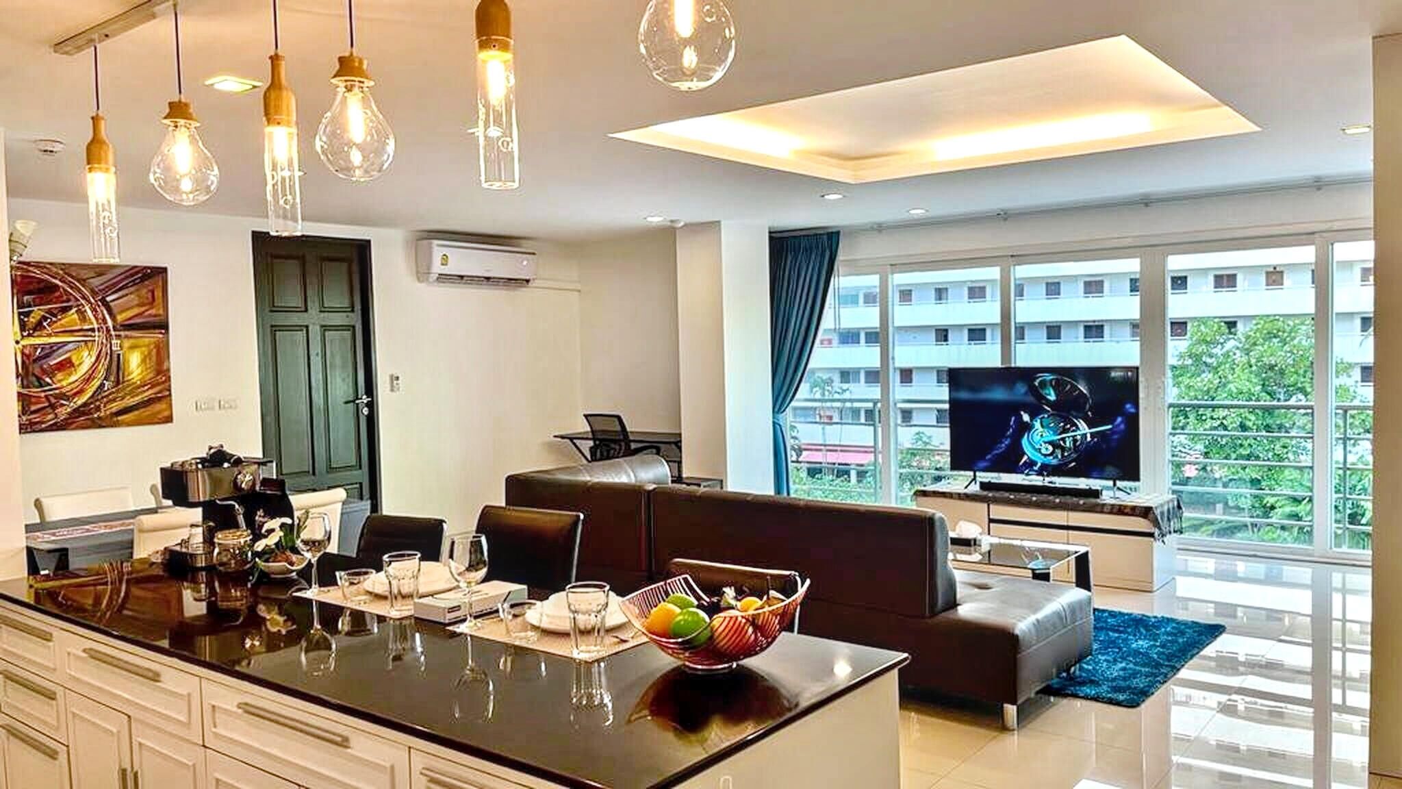 A modern living room with a kitchen island, dining area, and a large TV.