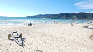 Une plage de sable fin, un ciel bleu azur, quelques personnes et une montagne en arrière-plan.