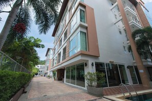 A modern building with a glass facade, a pool area, and a well-maintained garden with palm trees. - Haven Lagoon Condominium (Patong)