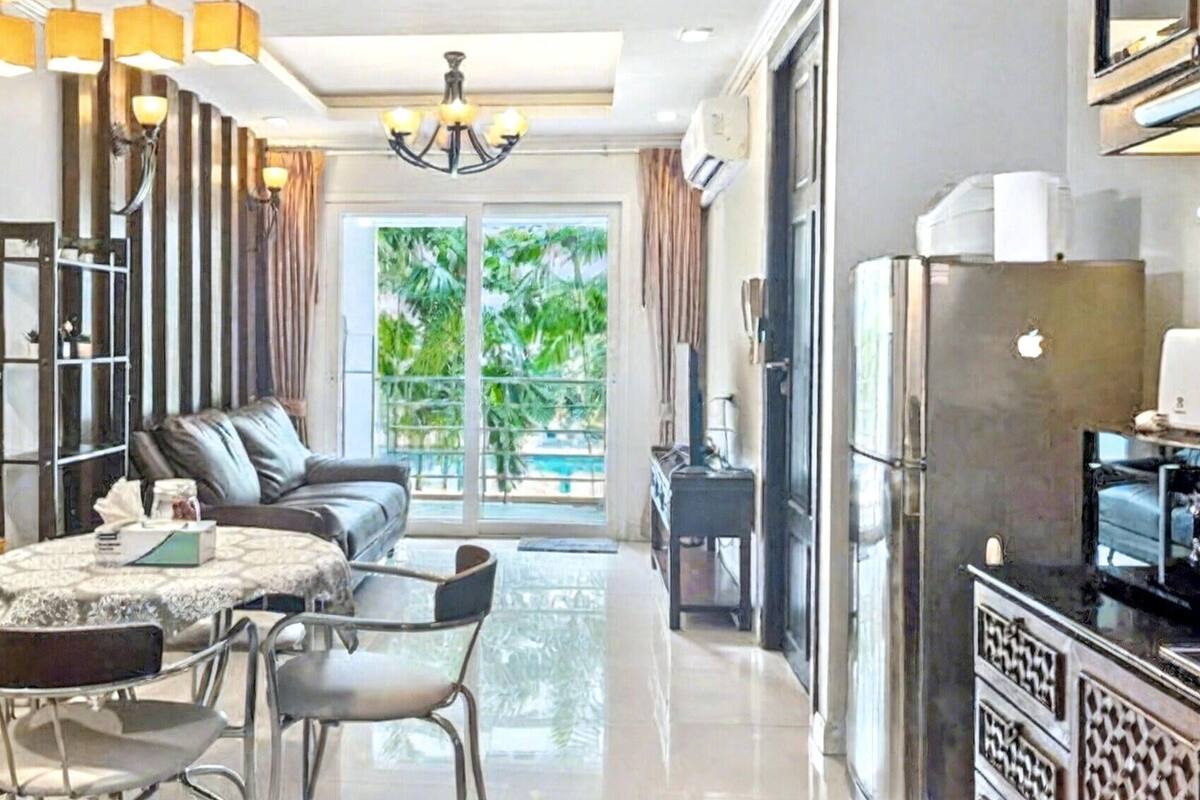 A modern kitchen with a dining area, a sofa, and a large window with a view of greenery.