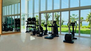 A gym with various exercise equipment, large windows, and a view of palm trees and the ocean.