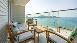 A balcony with wooden furniture, a view of the sea, and a Ferris wheel in the distance.