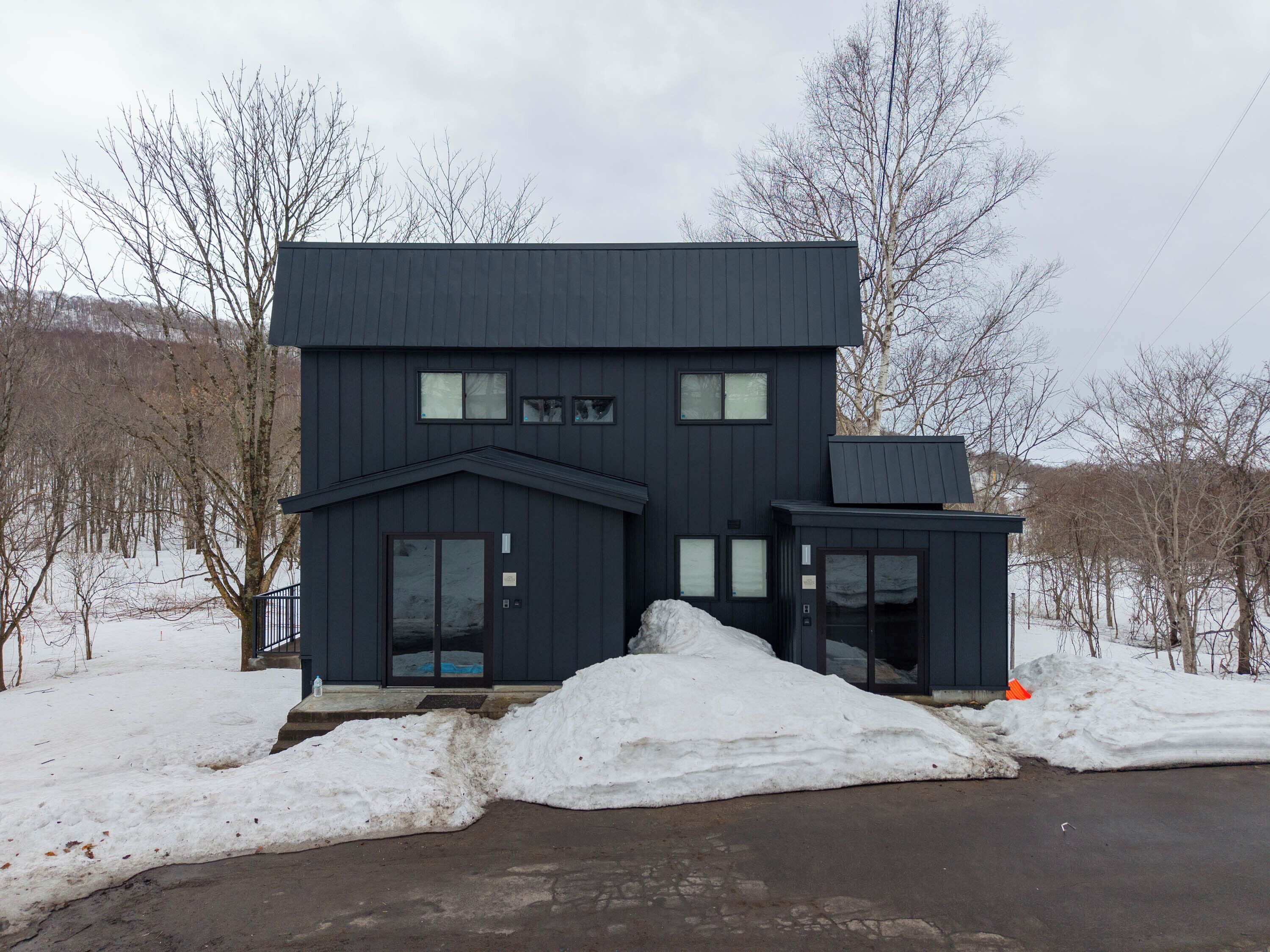 A two-story building with a dark exterior, large windows, and a small attached structure.