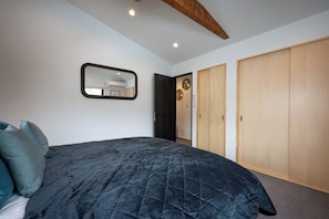A bedroom with a dark quilted bedspread, a mirror on the wall, a wooden ceiling beam, and a wardrobe with a light wood finish. - Niseko Town, Toyosato A near Hirafu, Niseko village and 30' Risutsu (Niseko-cho)