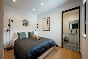 Une chambre à coucher avec un lit, des oreillers, un ours en peluche, une lampe sur pied, un miroir et un tableau encadré accroché au mur.