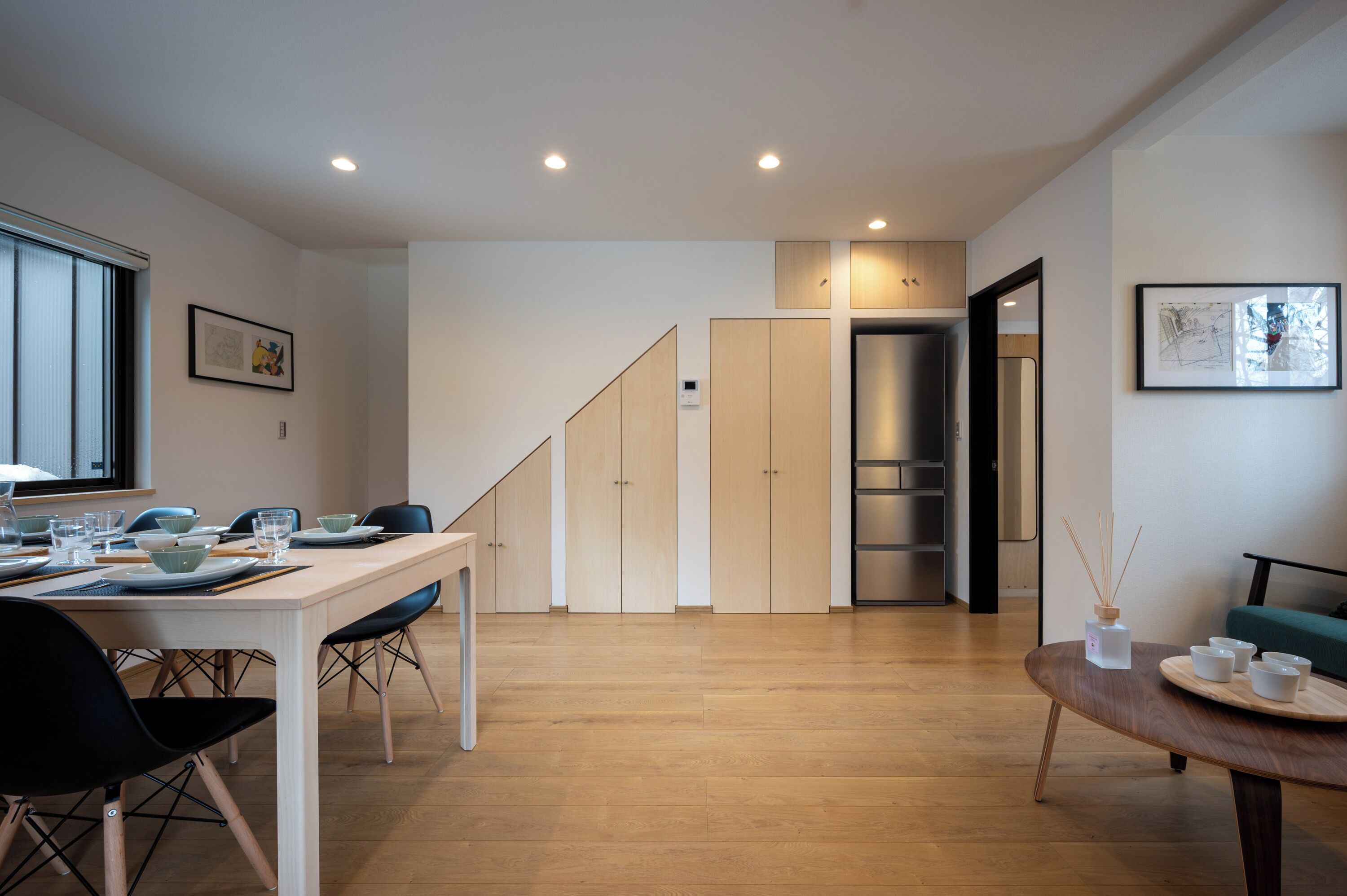 A modern kitchen with wooden cabinets, a dining table set with plates and glasses, and a staircase leading to another room.