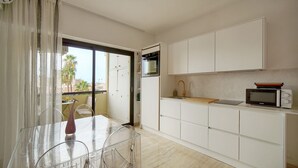 Una cocina moderna con armarios blancos, un microondas y un comedor con una mesa y sillas de vidrio.