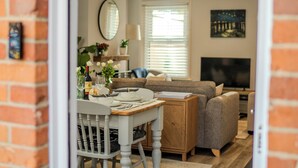 A dining area with a wooden table, chairs, and a sofa. There is a television in the background. - Stylish 2-bed house ideal for business & family stays, garden, free parking. (Southampton)