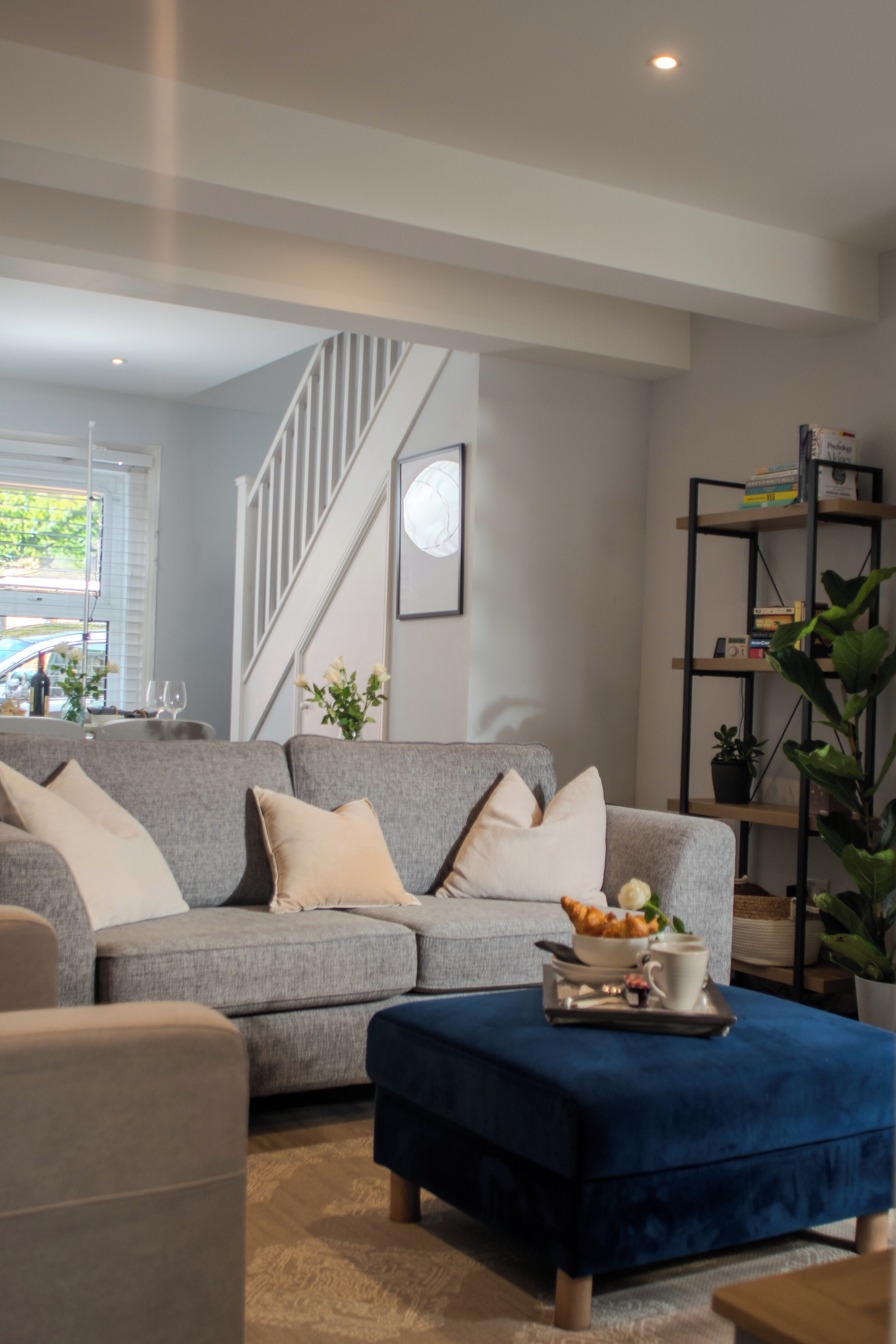 A modern living room with a grey sofa, a blue ottoman, and a bookshelf.