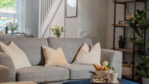 A modern living room with a grey sofa, a blue ottoman, and a bookshelf. - Stylish 2-bed house ideal for business & family stays, garden, free parking. (Southampton)