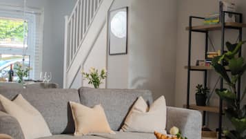 A modern living room with a grey sofa, a blue ottoman, and a bookshelf.