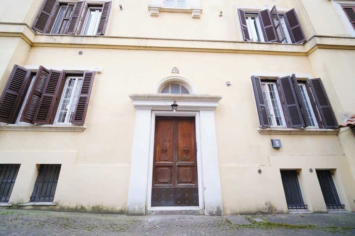 A building with a central wooden door, multiple windows with shutters, and a cobblestone ground.
