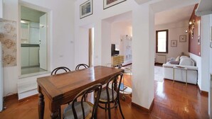Een eetgedeelte met een houten tafel en stoelen, een keuken op de achtergrond en een zithoek met een bank en een televisie.