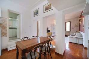 Un coin repas avec une table et des chaises en bois, une cuisine à l’arrière-plan et un espace de détente avec un canapé et un téléviseur.