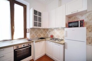 Une cuisine avec des meubles blancs, une cuisinière à gaz, un four à micro-ondes et un évier.