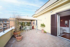 Un balcon agrémenté de plantes en pot, une table et des chaises, ainsi qu’une porte-fenêtre coulissante donnant sur un espace intérieur.