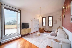 Uma sala de estar com sofá, banquinho, televisão e um armário branco.
