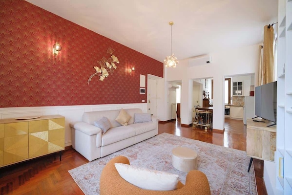 A living room with a sofa, ottoman, patterned rug, and a decorative wall piece.