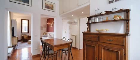 Un comedor con mesa y sillas de madera, un armario con utensilios de cocina y un cuadro en la pared.