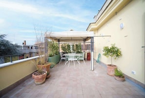 A rooftop terrace with a covered dining area, potted plants, and a view of the city.