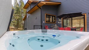 Un bain à remous avec une terrasse en bois et des chaises rouges, un barbecue et une fenêtre donnant sur une zone boisée.