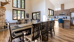 Un vaste espace dédié à la salle à manger, avec une grande table et des chaises en bois, une cheminée en pierre et de grandes fenêtres offrant une vue sur l’extérieur.