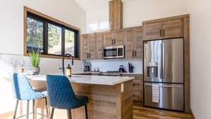 Une cuisine moderne avec des meubles en bois, un réfrigérateur en acier inoxydable, un four à micro-ondes et un coin bar avec des chaises bleues.