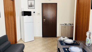 A compact kitchen with a refrigerator, microwave, and a small countertop. There is a dining table set with plates and cutlery.