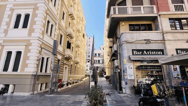 A street view with a narrow road flanked by multi-story buildings, including a hotel and a bar.